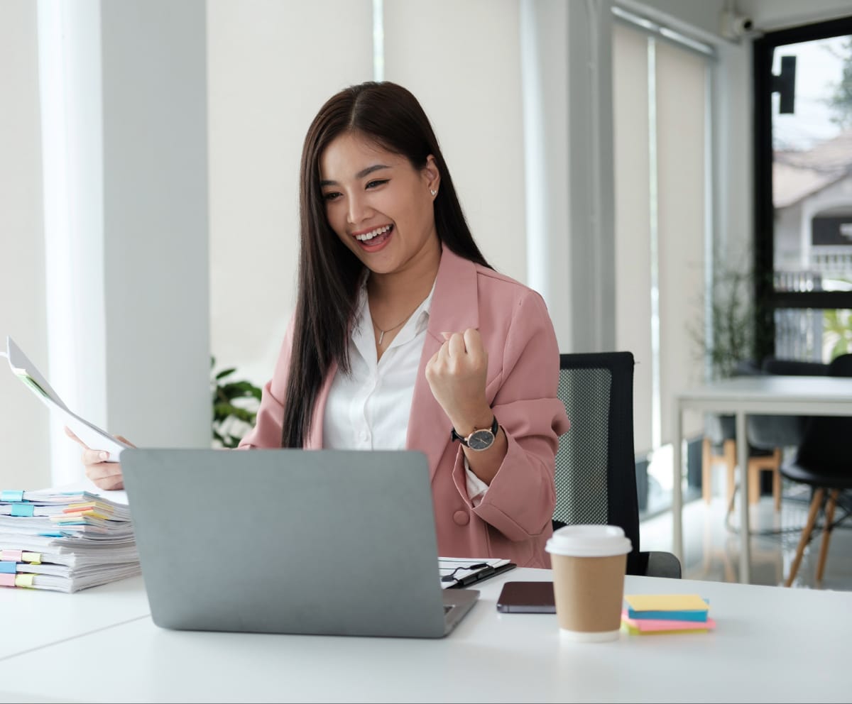 Woman smiles and punches fist whilst looking at laptop